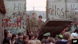 East German border guards look through a hole in the Berlin wall after demonstrators pulled down one segment of the wall at Brandenburg gate Saturday, November 11, 1989. (AP Photo/Lionel Cironneau)