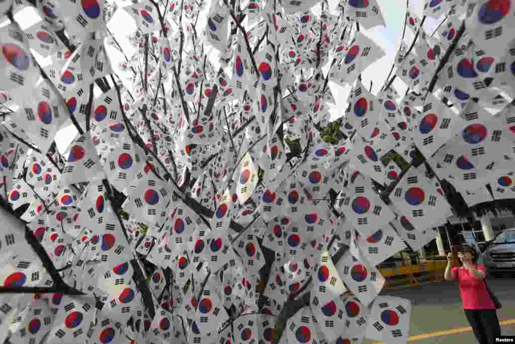 A woman takes a photograph of a tree decorated with national flags at the national cemetery in Seoul on the eve of South Korea&#39;s Memorial Day to commemorate fallen patriots.