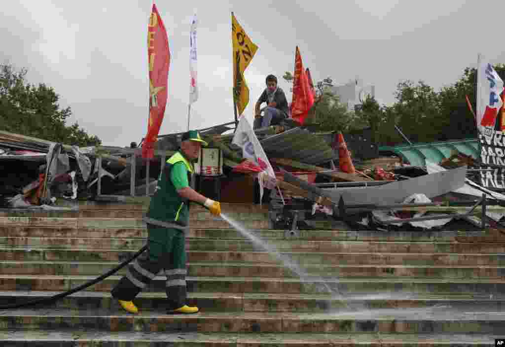 A municipality worker cleans with water the steps of Taksim Square as a protester sits on a barricade, Istanbul, June 13, 2013.