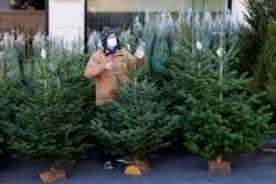 Seorang penjual pohon Natal di pasar terbuka di Nice, Prancis, mengenakan masker pelindung saat menunggu pembeli, 14 Desember 2021. (REUTERS/Eric Gaillard)