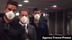 This screen grab taken from AFPTV shows Serbia's Novak Djokovic (C) preparing to depart from Melbourne Airport in Melbourne on Jan. 16, 2022, after losing a sensational legal battle over his coronavirus vaccination status. (Photo by Mell Chun / AFP) 