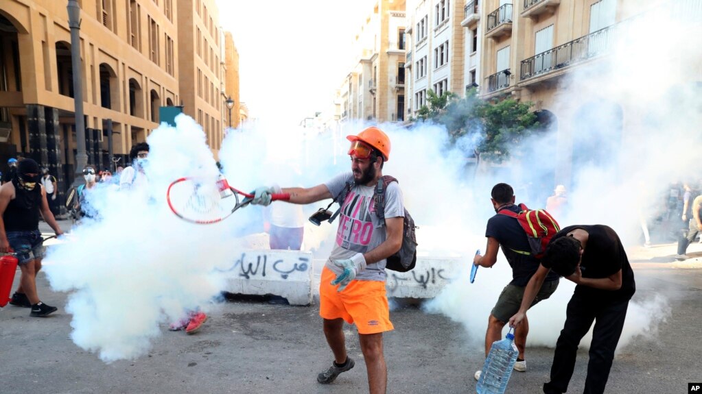An anti-government protester uses a a tennis racket to hit back a tear gas canister towards at riot policemen during a protest following last Tuesday's massive explosion which devastated Beirut, Lebanon, Monday, Aug. 10, 2020. 