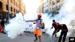 An anti-government protester uses a a tennis racket to hit back a tear gas canister towards at riot policemen during a protest following last Tuesday's massive explosion which devastated Beirut, Lebanon, Monday, Aug. 10, 2020. 