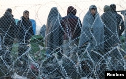 Migrants stand behind a border fence at the Greek-Macedonian border, after additional passage restrictions imposed by Macedonian authorities left hundreds of them stranded near the village of Idomeni, Greece, Feb. 23, 2016.