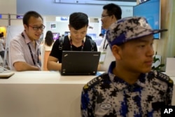 FILE - Visitors use a laptop computer at a display booth as a security guard stands nearby at the Global Mobile Internet Conference in Beijing, April 29, 2015.