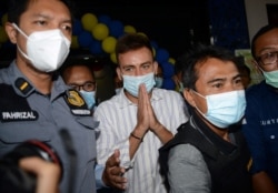 Sergey Kosenko (tengah) warga negara Rusia, dikawal dari kantor imigrasi ke Bandara Ngurah Rai di Jimbaran, Bali, 24 Januari 2021. (Foto: SONNY TUMBELAKA / AFP)