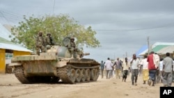 FILE - In this photo provided by the African Union Mission to Somalia (AMISOM), African Union (AU) soldiers from Uganda sit on their tank as residents walk past in the town of Bulomarer, in the Lower Shabelle region of Somalia, Aug. 31, 2014.