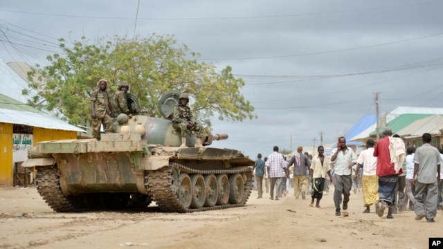 FILE - In this photo provided by the African Union Mission to Somalia (AMISOM), African Union (AU) soldiers from Uganda sit on their tank as residents walk past in the town of Bulomarer, in the Lower Shabelle region of Somalia, Aug. 31, 2014.