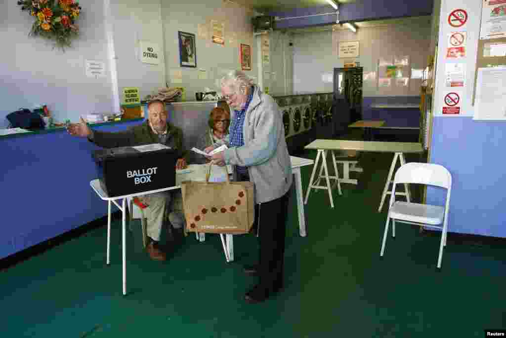 A man receives his voting paper from poll clerks in a public launderette being used as a polling station in Oxford, May 7, 2015.