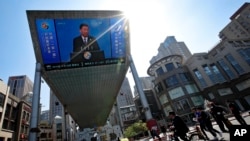 People pass by a TV screen broadcasting live President Xi Jinping's opening speech, outside a shopping mall in Beijing, April 26, 2019. 