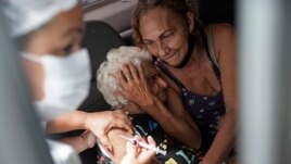 An elderly woman gets a shot of China's Sinovac CoronaVac vaccine as part of a priority COVID-19 vaccination program for the elderly at a drive-thru vaccination center in Rio de Janeiro, Brazil, Monday, Feb. 1, 2021.