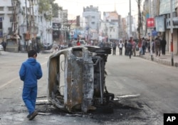 FILE - A boy walks past a vehicle burnt by a mob during a protest against Thursday's attack on a paramilitary convoy, in Jammu, India, Feb. 15, 2019.
