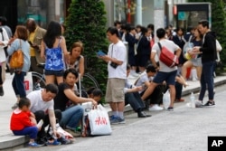 资料照：中国游客在日本东京银座购物后坐在人行道路牙上休息。（2015年5月6日）