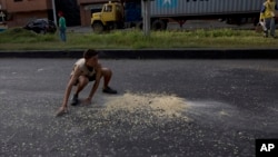 FILE - A youth moves quickly to collect grains of corn on the street that fell from a truck that was looted outside the port in Puerto Cabello, Venezuela, Jan. 23, 2018.