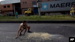 En esta foto de archivo, un joven recoge granos de maíz en la calle que cayeron de un camión saqueado en las afueras de Puerto Cabello, Venezuela. Enero 23 de 2018.