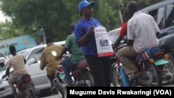 A stream of boda bodas passes a woman holding a poster advertising the launch of a new VOA frequency in Juba in March 2013.