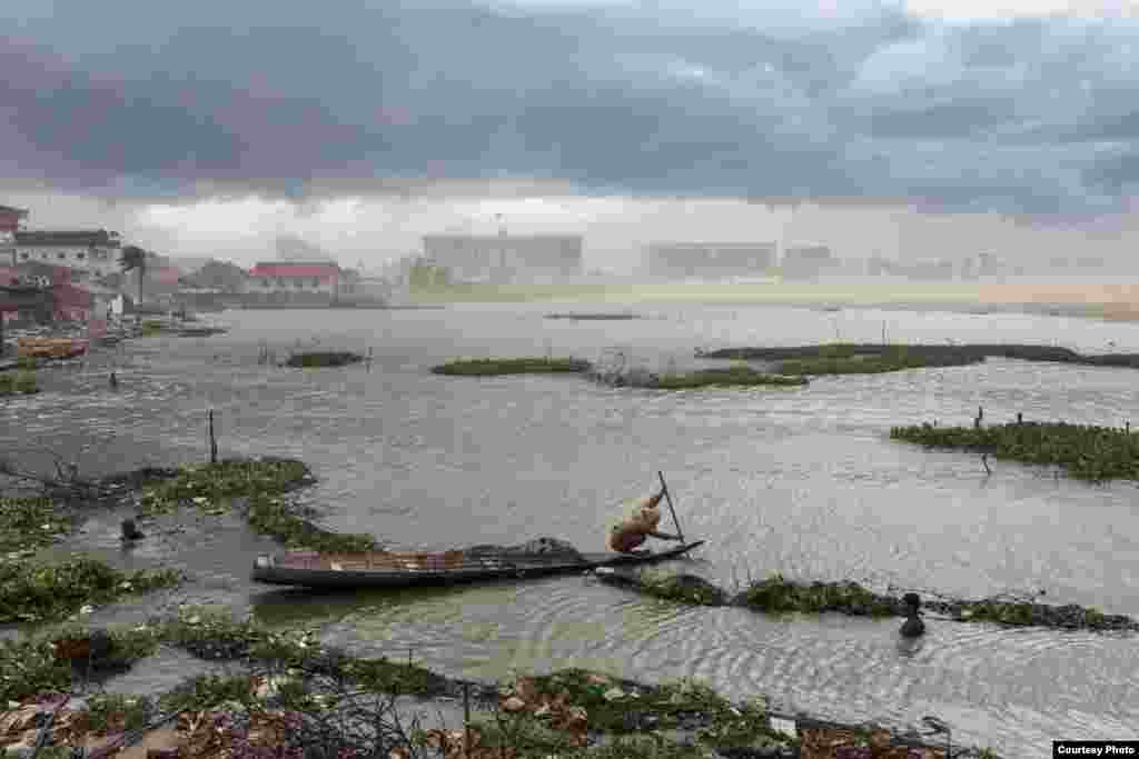 July 07, 2011 - Phnom Penh, Cambodia. A resident of Boeung Kak rows a wooden boat against a storm moving in over Phnom Penh. The new buildings of the Council of Ministers and the office of the Prime Minister can be seen in the background. &copy; Nicolas Axelrod / Ruom