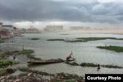 July 07, 2011 - Phnom Penh, Cambodia. A resident of Boeung Kak rows a wooden boat against a storm moving in over Phnom Penh. The new buildings of the Council of Ministers and the office of the Prime Minister can be seen in the background. © Nicolas Axelro