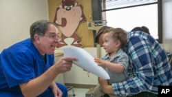 Dr. Charles Goodman, left, explains to Frank Fierro, the father of 1 year-old Cameron Fierro, the need of getting the measles-mumps-rubella vaccine, or MMR vaccine at his practice in Northridge, Calif., Thursday, Jan. 29, 2015. (AP Photo/Damian Dovarganes)