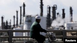 FILE - A worker cycles near a factory at the Keihin industrial zone in Kawasaki, Japan, Feb. 17, 2016. A survey released Tuesday showed 83 percent of private equity firms are concerned about the impact climate change could have on the businesses they invest in.