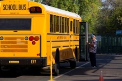 Seorang karyawan menunggu untuk membantu seorang siswa turun dari bus saat pembelajaran langsung dilanjutkan dengan pembatasan untuk mencegah penyebaran Covid-19) di Sekolah Dasar Rover di Tempe, Arizona, AS, 17 Agustus 2020. (Foto: Reuters)