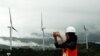 FILE - A woman takes pictures of wind power plant propeller blades in Sidenreng Rappang, Sulawesi Island, Indonesia, Jan. 15, 2018. 