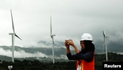 FILE - A woman takes pictures of wind power plant propeller blades in Sidenreng Rappang, Sulawesi Island, Indonesia, Jan. 15, 2018.