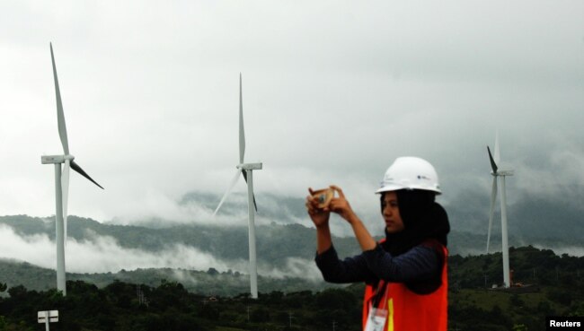 FILE - A woman takes pictures of wind power plant propeller blades in Sidenreng Rappang, Sulawesi Island, Indonesia, Jan. 15, 2018.