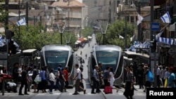 FILE - Pedestrians cross a street next to the light rail trams in Jerusalem, May 11, 2017. Rights groups are criticizing the involvement of French companies in the building of another tram that connects to Israeli settlements. 