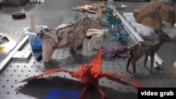 Examples of creatures folded out of paper by Robert Salazar are spread out on a workbench in this image taken from video. (E. Lee/VOA)