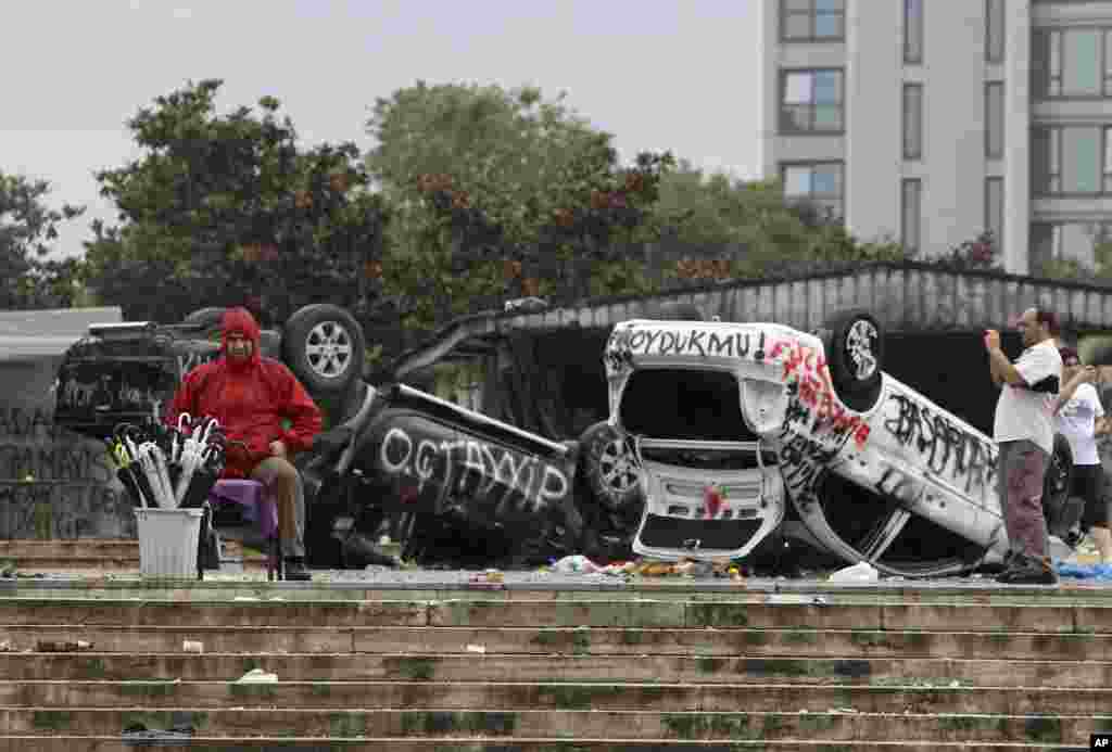 A street vendor sells umbrellas in front of destroyed police cars at the Taskim square in Istanbul, Turkey. Protests in Istanbul and several other Turkish cities appear to have subsided, after days of fierce clashes following a police crackdown on a peaceful gathering as protesters denounced what they see as Prime Minister Recep Tayyip Erdogan&#39;s increasingly authoritarian style.