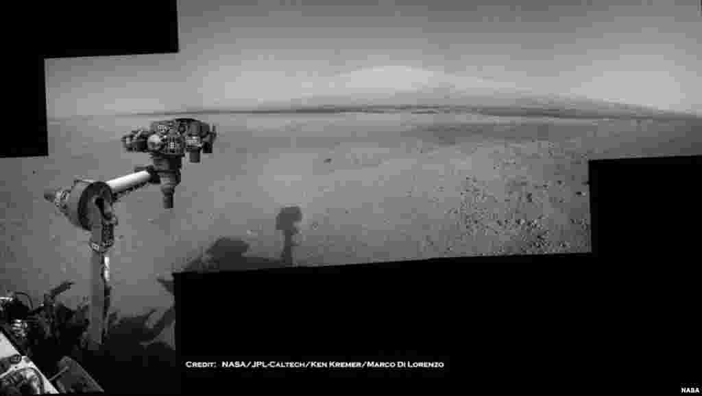 The Mars Curiosity rover's robotic arm takes aim at Mount Sharp in a mosaic that combines navigation-camera imagery from Sols 2, 12 and 14 (Aug. 8, 18 and 20). The shadow of the rover's camera mast is visible in the center foreground.
