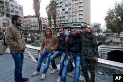 Syrian men pose for a picture as they gather in the Marjeh square in Damascus, Syria, Tuesday, Feb. 23, 2016. The Syrian government and the main umbrella for Syrian opposition and rebel groups announced on Tuesday they both conditionally accept a proposed U.S.-Russian cease fire that the international community hopes will bring them back to the negotiating table in Geneva for talks to end the war.