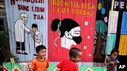 Anak-anak bermain di dekat mural di perkampungan untuk warga berpenghasilan rendah di Jakarta, 4 Agustus 2020. (AP Photo/Dita Alangkara)