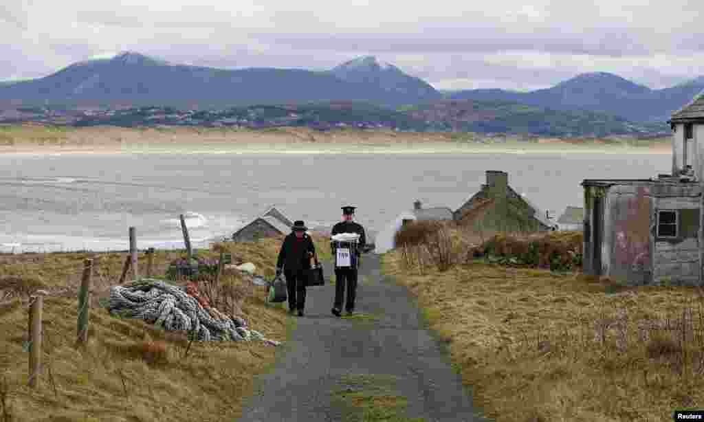 Bà Carmel McBride (trái) và Trung sĩ Paul McGee đi khỏi phòng bỏ phiếu để rời đi bằng máy bay trực thăng từ đảo Inishbofin, ở Ireland. Hòn đảo này, nằm ngoài khơi bờ biển Donegal, bỏ phiếu một ngày trước đại lục cho cuộc tổng tuyển cử.