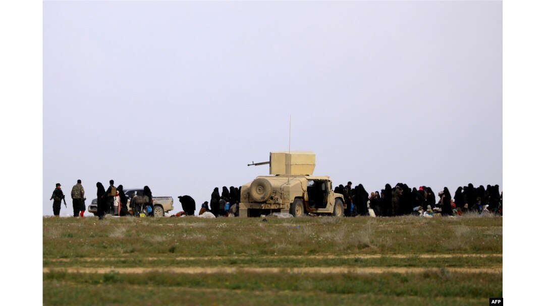 Fighters of the Syrian Democratic Forces (SDF) accompany women and children as they wait in a field after fleeing the Islamic State (IS) group's last holdout of Baghuz in Syria, Feb. 21, 2019.