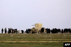 Fighters of the Syrian Democratic Forces (SDF) accompany women and children as they wait in a field after fleeing the Islamic State (IS) group's last holdout of Baghuz in Syria, Feb. 21, 2019.