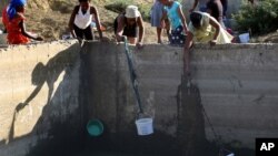 Women use buckets and cloth to collect stagnant rain water from an unfinished sewerage treatment tank, now used as a well, to do their laundry in Senekal, South Africa where taps and water sources have run dry, Jan. 7, 2016.