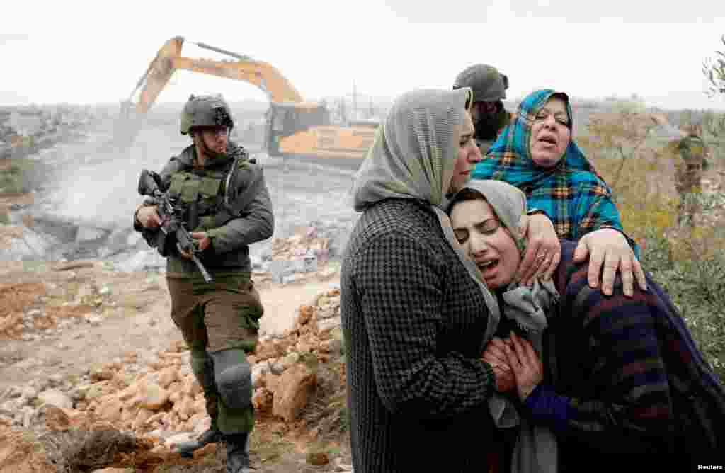 A Palestinian woman is comforted as she reacts while Israeli machinery demolishes her under-construction house, in Hebron, in the Israeli-occupied West Bank.