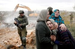A Palestinian woman is comforted as she reacts while Israeli machinery demolishes her under-construction house, in Hebron, in the Israeli-occupied West Bank, Dec. 28, 2021.