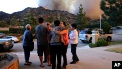 Una familia se conforta luego de evacuar su casa mientras los bomberos combaten las llamas en Azusa, California.