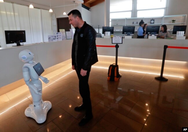 FILE - A guest from Moldavia asks robot Robby Pepper for information at the front desk of hotel in Peschiera del Garda, northern Italy, March 12, 2018. The hotel uses the robot to assist guests.