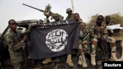 FILE - Nigerian soldiers hold up a Boko Haram flag that they had seized in the retaken town of Damasak, Nigeria, March 18, 2015. 