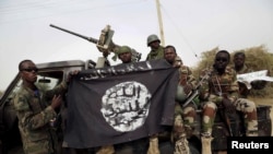 Des soldats nigérians brandissent un drapeau Boko Haram qu'ils ont saisi dans la ville reprise de Damasak, au Nigeria, le 18 mars 2015.