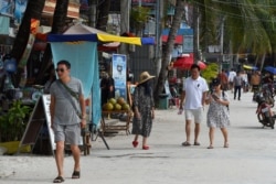 FILE - Tourists walk along a beach on Koh Rong island in Sihanoukville province on October 31, 2019. (Photo by TANG CHHIN Sothy / AFP)