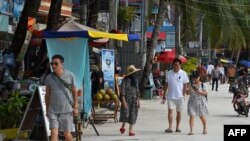 FILE - Tourists walk along a beach on Koh Rong island in Sihanoukville province on October 31, 2019. (Photo by TANG CHHIN Sothy / AFP)