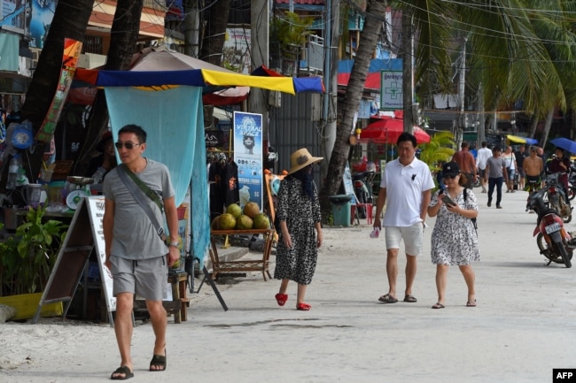 FILE - Tourists walk along a beach on Koh Rong island in Sihanoukville province on October 31, 2019. (Photo by TANG CHHIN Sothy / AFP)
