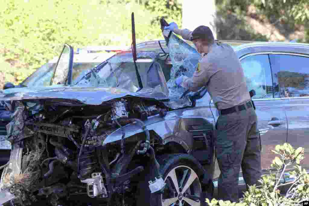 A law enforcement officer inspects a damaged vehicle following a rollover accident involving golfer Tiger Woods, Feb. 23, 2021, in the Rancho Palos Verdes suburb of Los Angeles, California. Woods suffered leg injuries in the one-car accident and was undergoing surgery, authorities and his manager said.