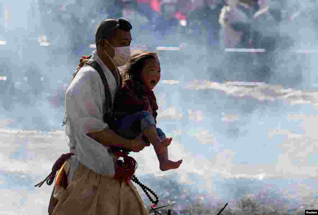 A Buddhist monk wearing a protective mask carries a child as he walks across smoldering hot ground at the fire-walking festival, called hiwatari matsuri in Japanese, at Mt.Takao in Tokyo, Japan, March 14, 2021.