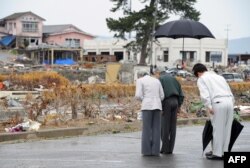 Gubernur Prefektur Fukushima Yuhei Sato (kedua dari kanan tersembunyi di belakang) memegang paying saat Kaisar Akihito (kedua dari kiri) dan Permaisuri Michiko (kiri) berdoa ketika mengunjungi wilayah yang dilanda tsunami di Soma, Prefektur Fukushima.